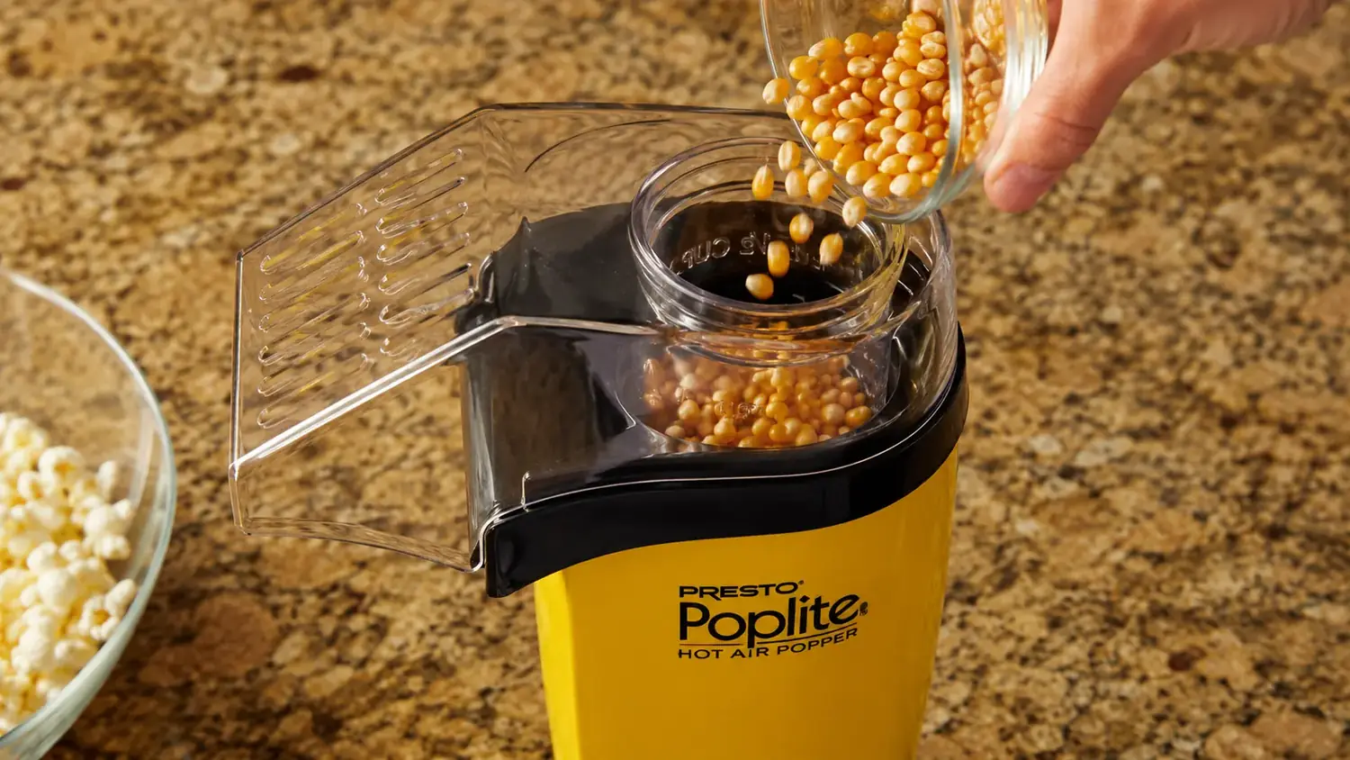A hand pouring popcorn kernels into the measuring cup on top of a hot-air popcorn popper
