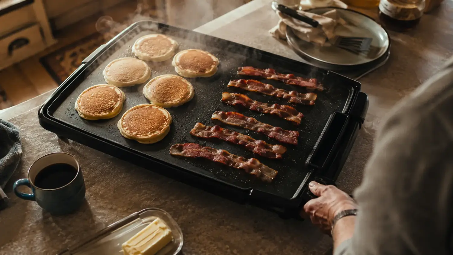 Presto 22-inch electric griddle sitting on a kitchen counter with pancakes cooking on one side and bacon on the other